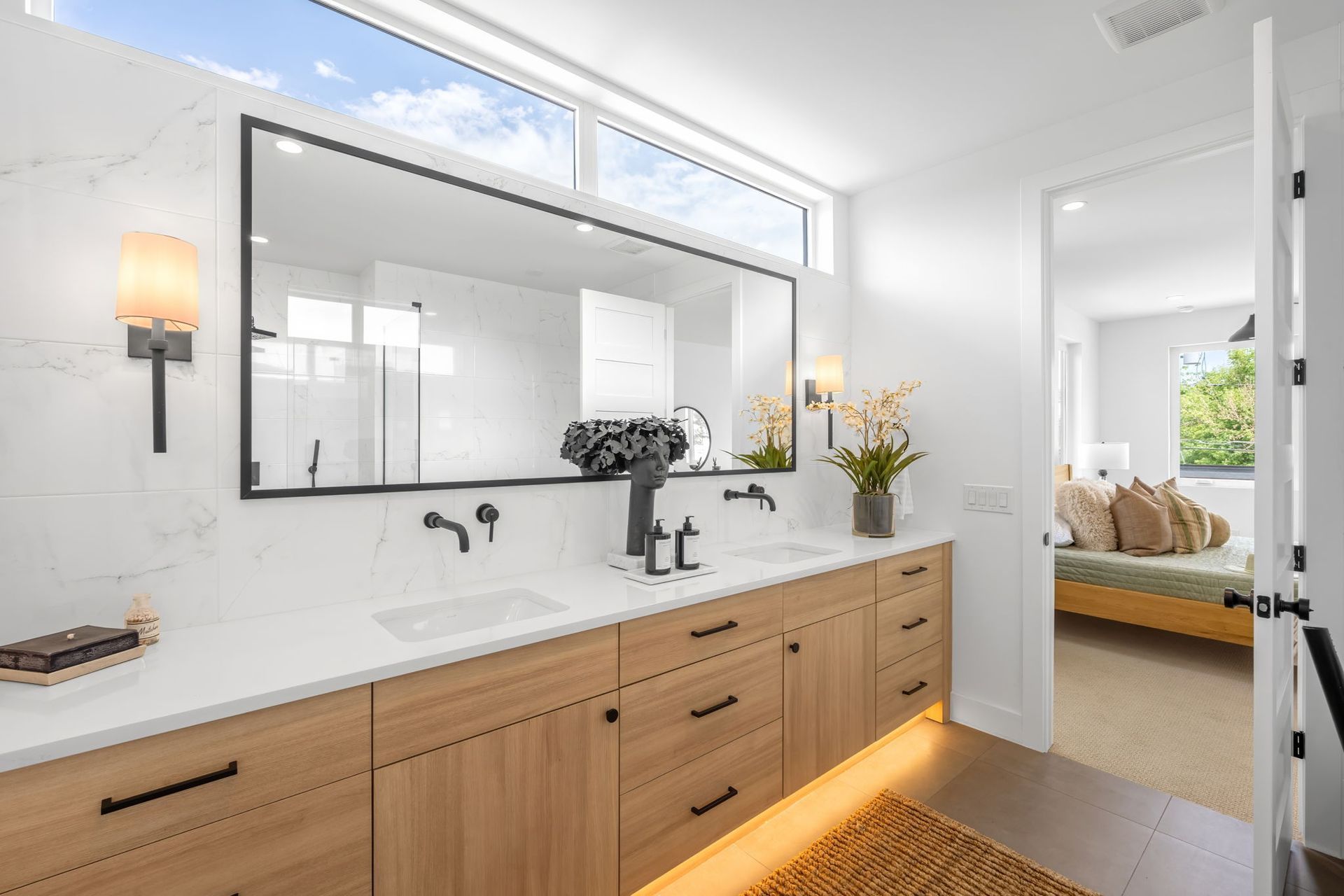 Modern bathroom with double vanity, large mirror, and open doorway to a bedroom.