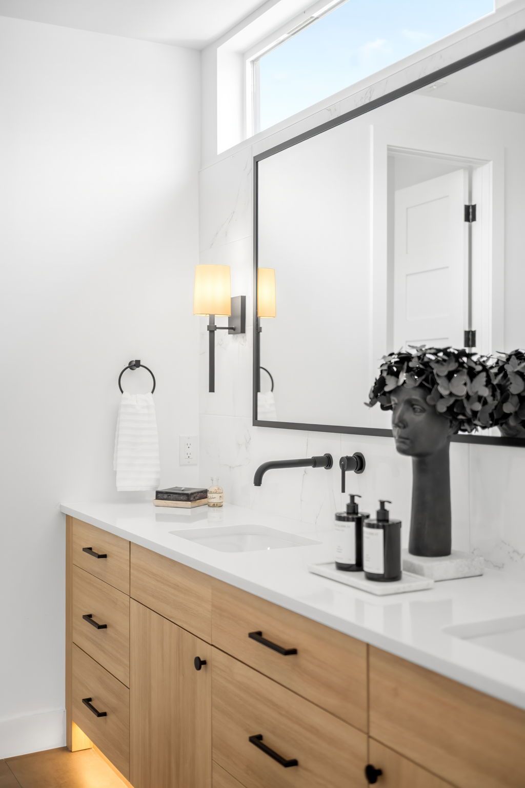 Modern bathroom with light wood vanity, black fixtures, large mirror, and white countertop.