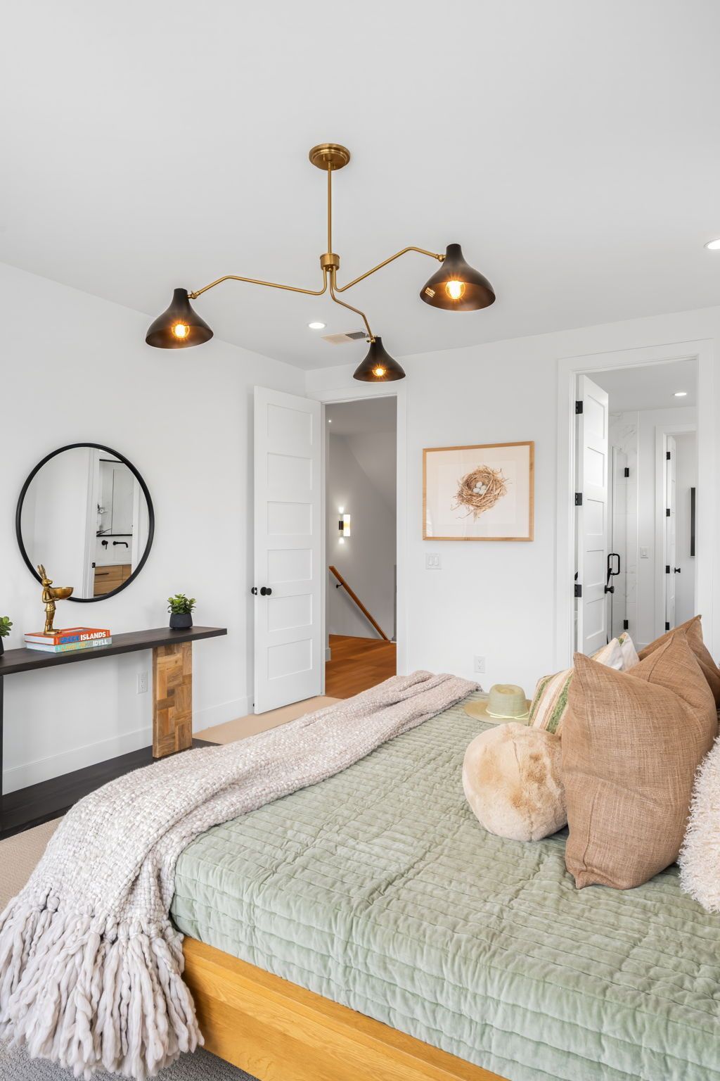 Bedroom with bed, pendant light fixture, side table, and round mirror.