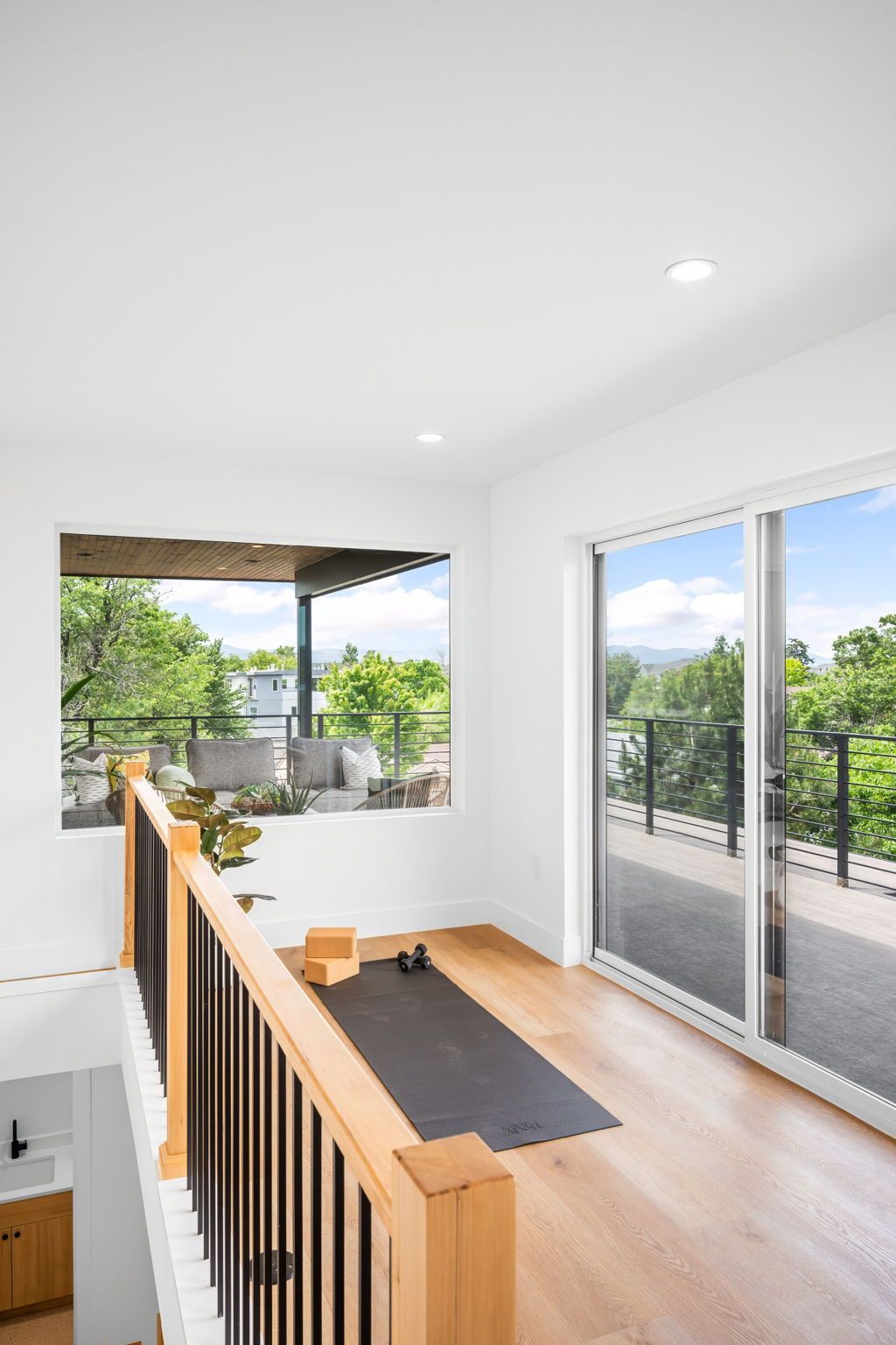 Bright yoga room with wooden floors, large window and sliding glass door with a balcony view.