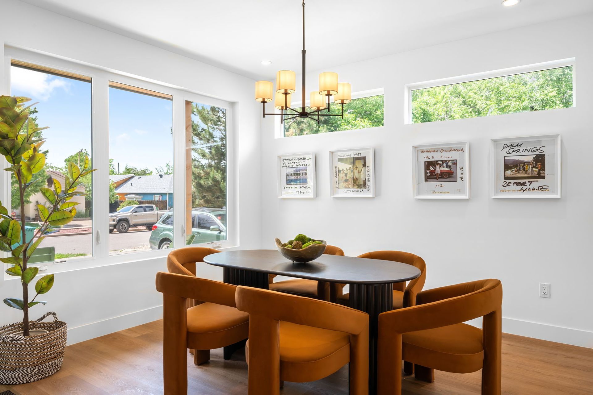 Dining room with oval table, orange chairs, and a window with a street view.  Artwork on the wall.