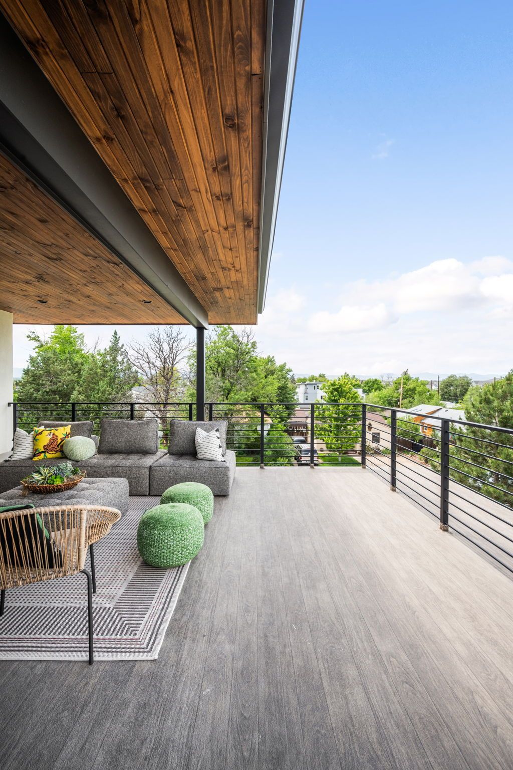 Outdoor patio with gray flooring, seating, wood ceiling, and a view of green trees.