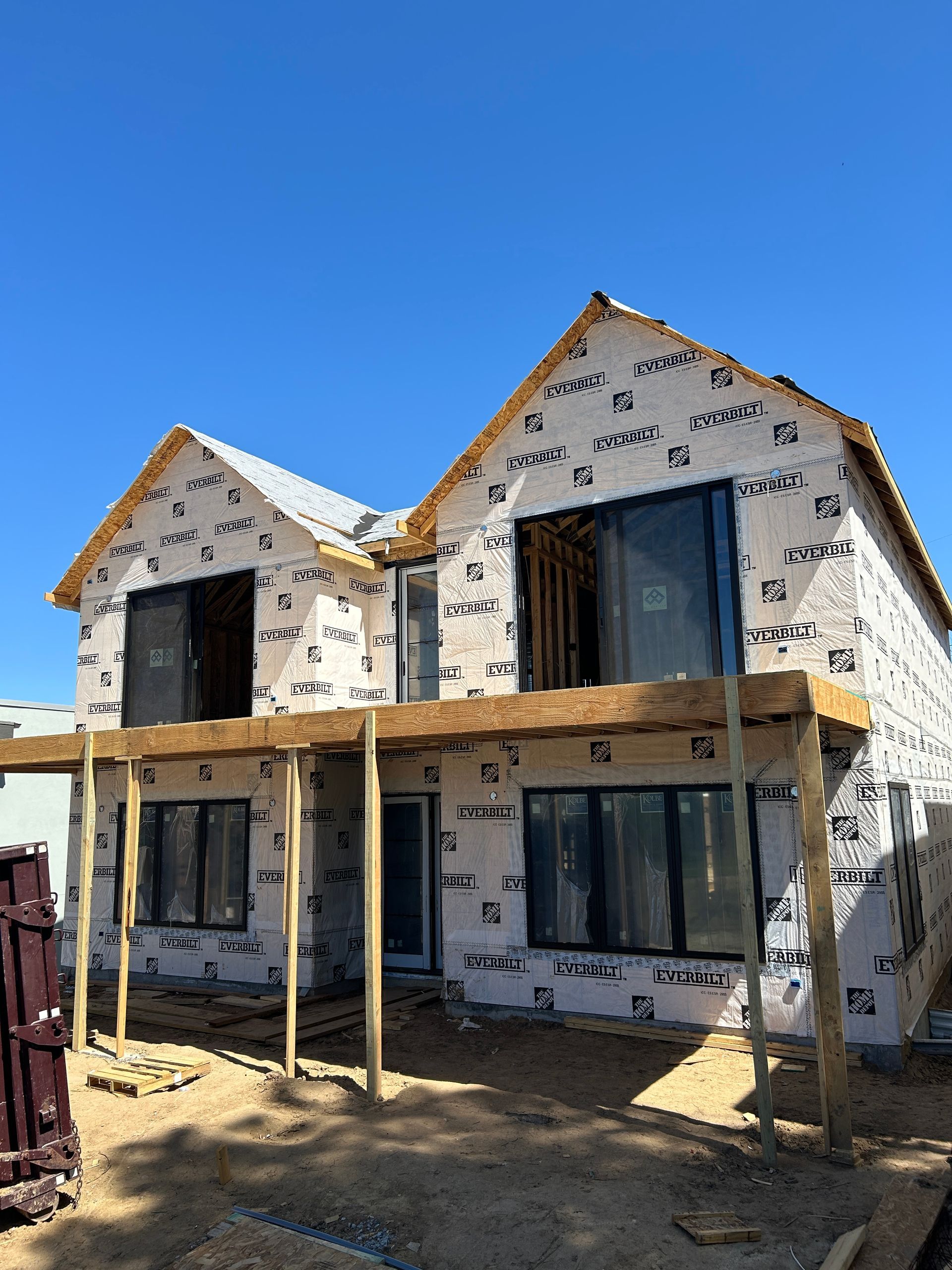 Two-story house under construction, wrapped in black and white material, with a wooden porch.