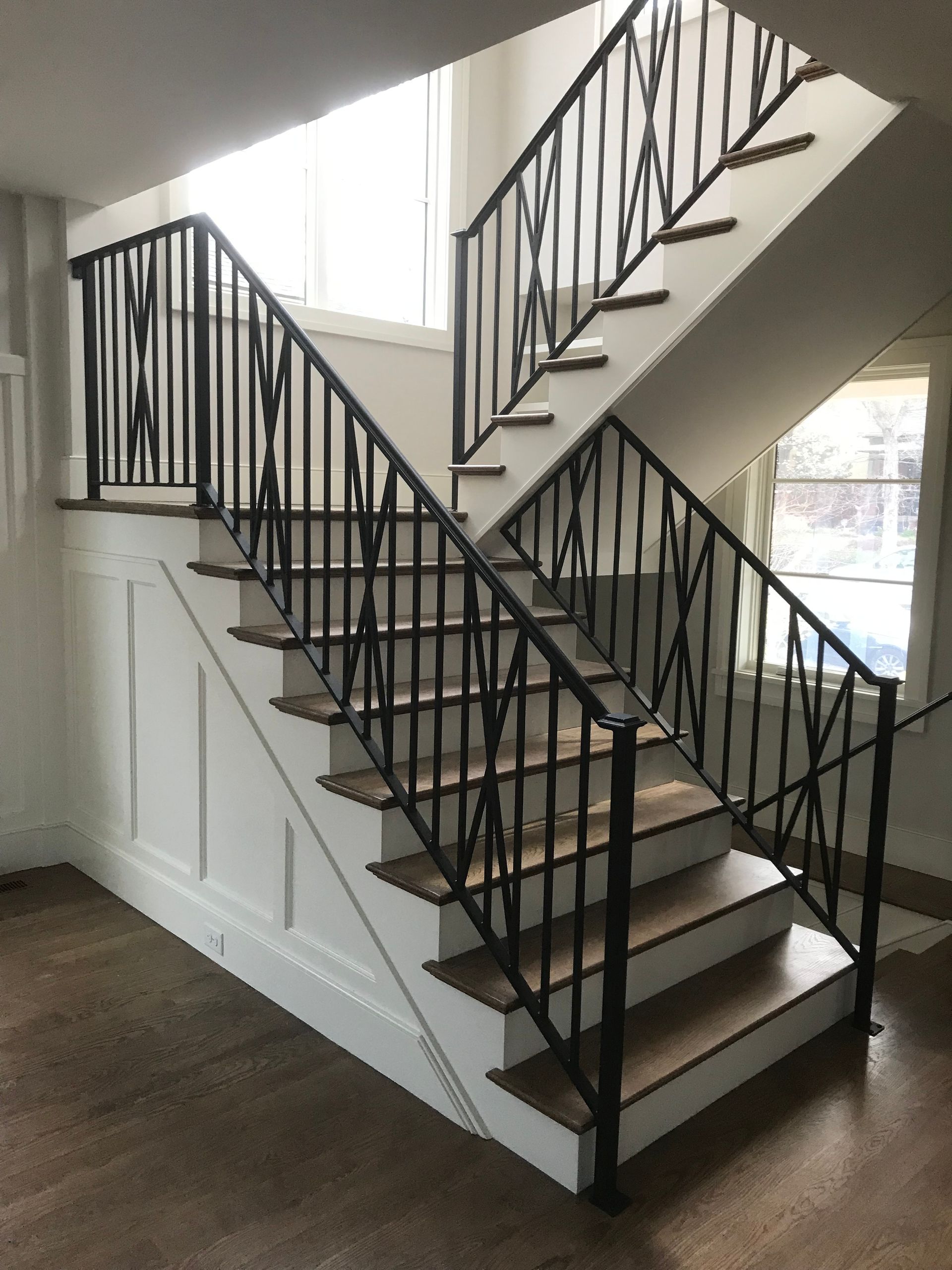 Staircase with black iron railing, wooden steps, and white wall paneling.