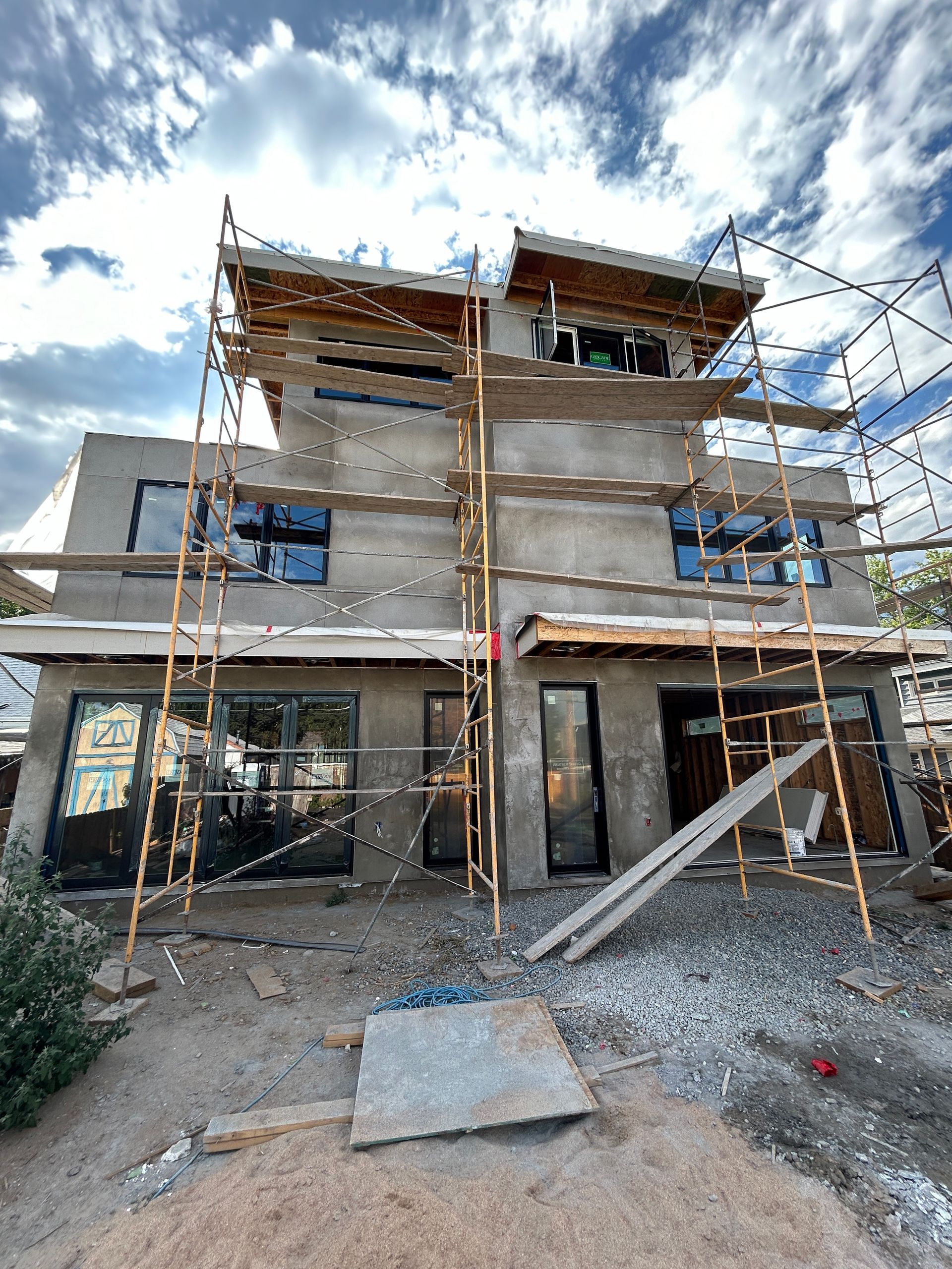 A two-story building under construction with scaffolding and a cloudy sky.