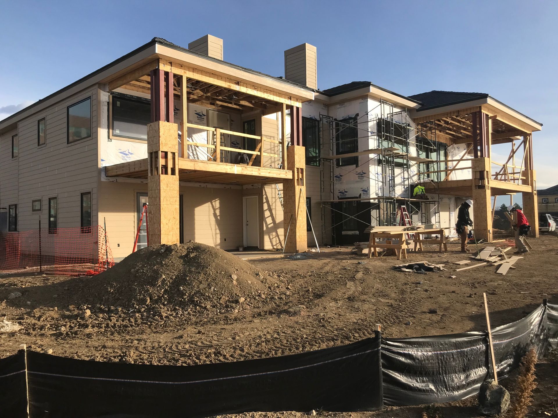 House under construction with exposed wood framing and scaffolding. Dirt and black barrier in foreground.
