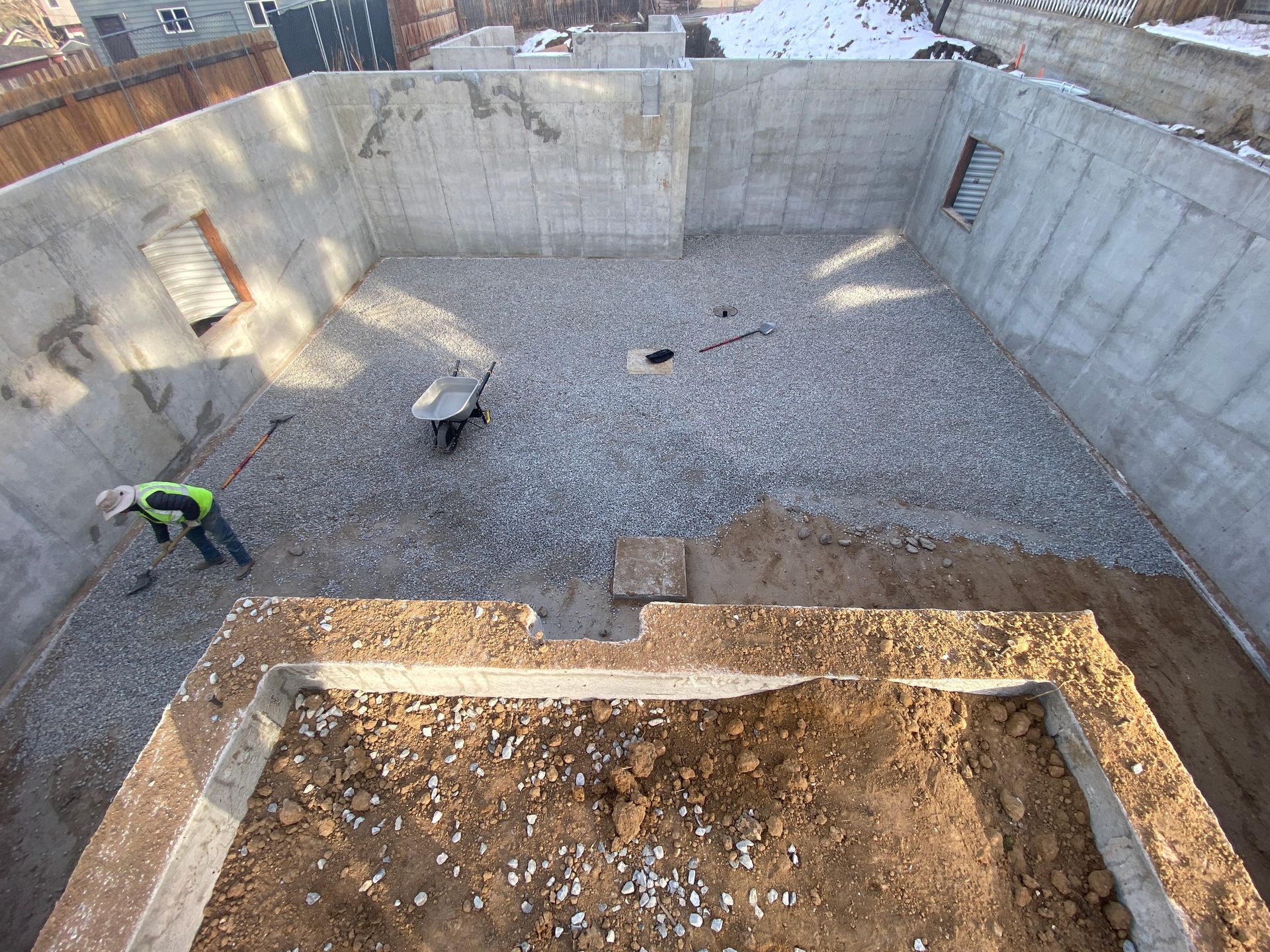 Construction site: concrete foundation with gravel base, worker, and dirt trench.