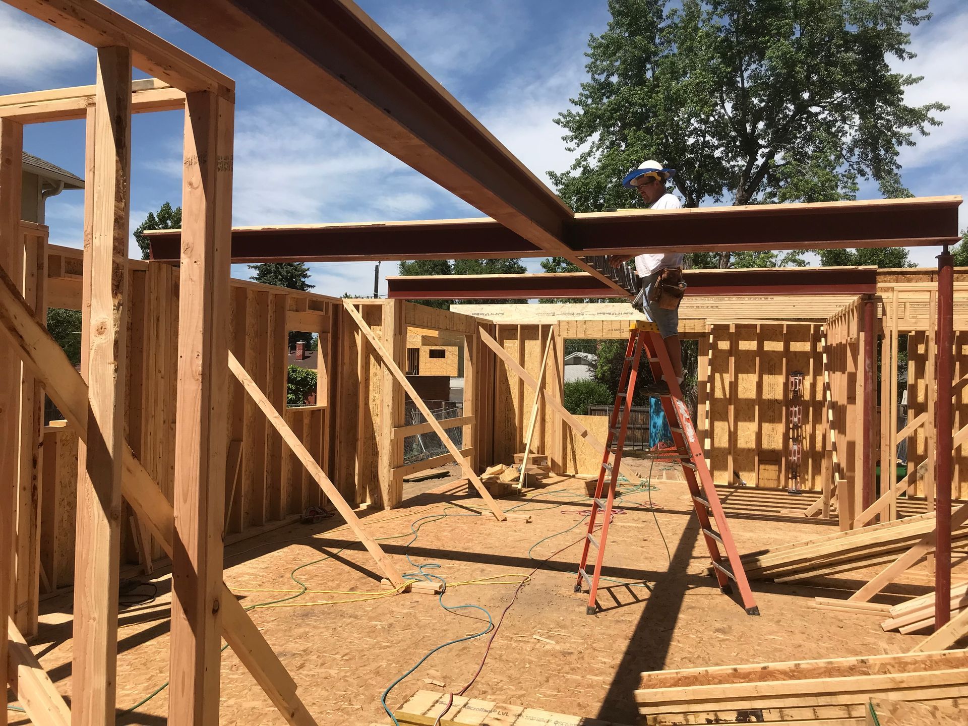 Construction worker on ladder, installing metal beam on wooden frame of a new building.