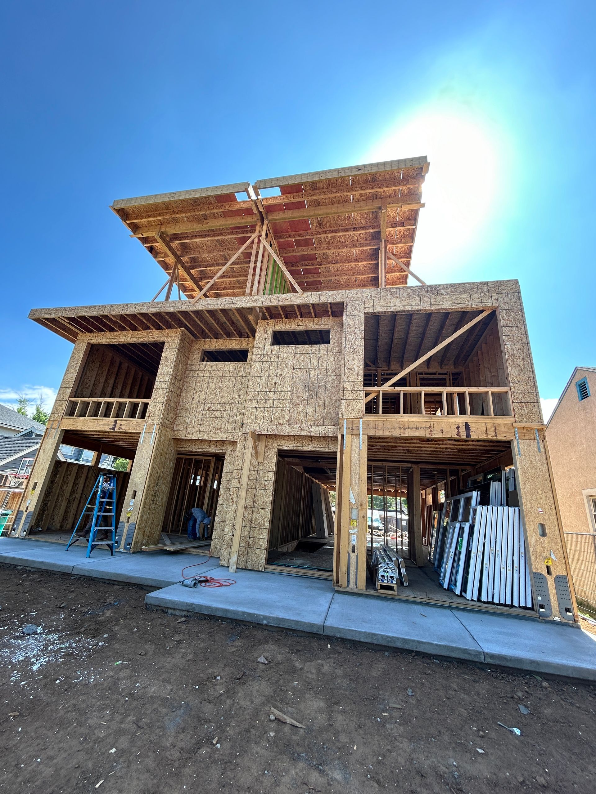 Construction of a two-story wooden house under a bright blue sky.
