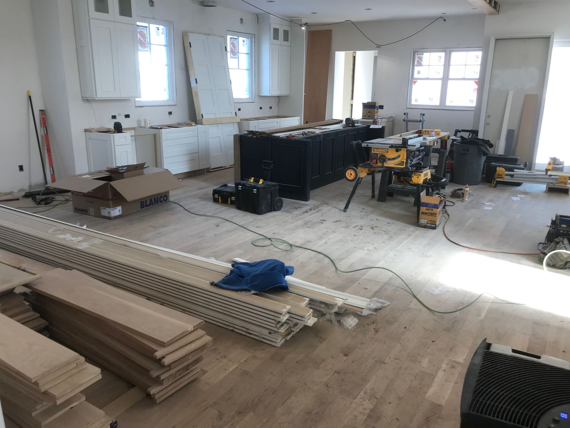 Room under construction with hardwood flooring, cabinets, tools, and materials scattered around.