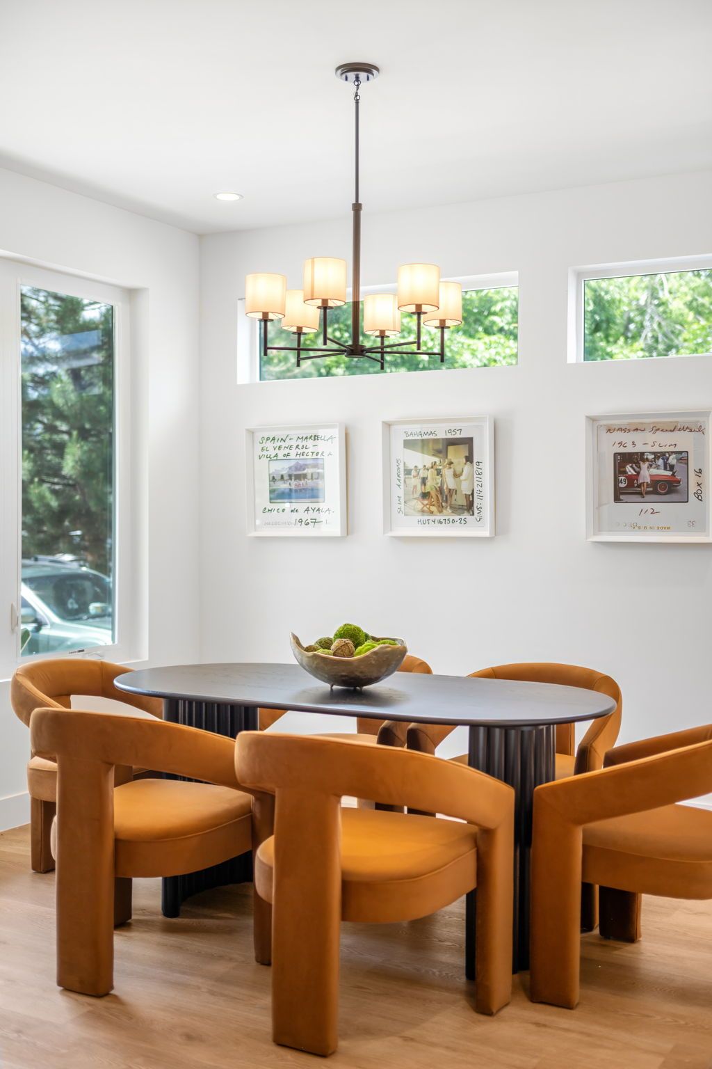 Dining room with oval table, mustard chairs, artwork, and modern chandelier.