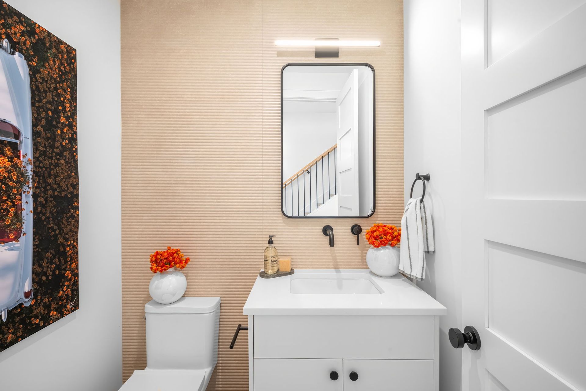 Powder room with light wood textured wall, white vanity, black framed mirror, and orange floral accents.
