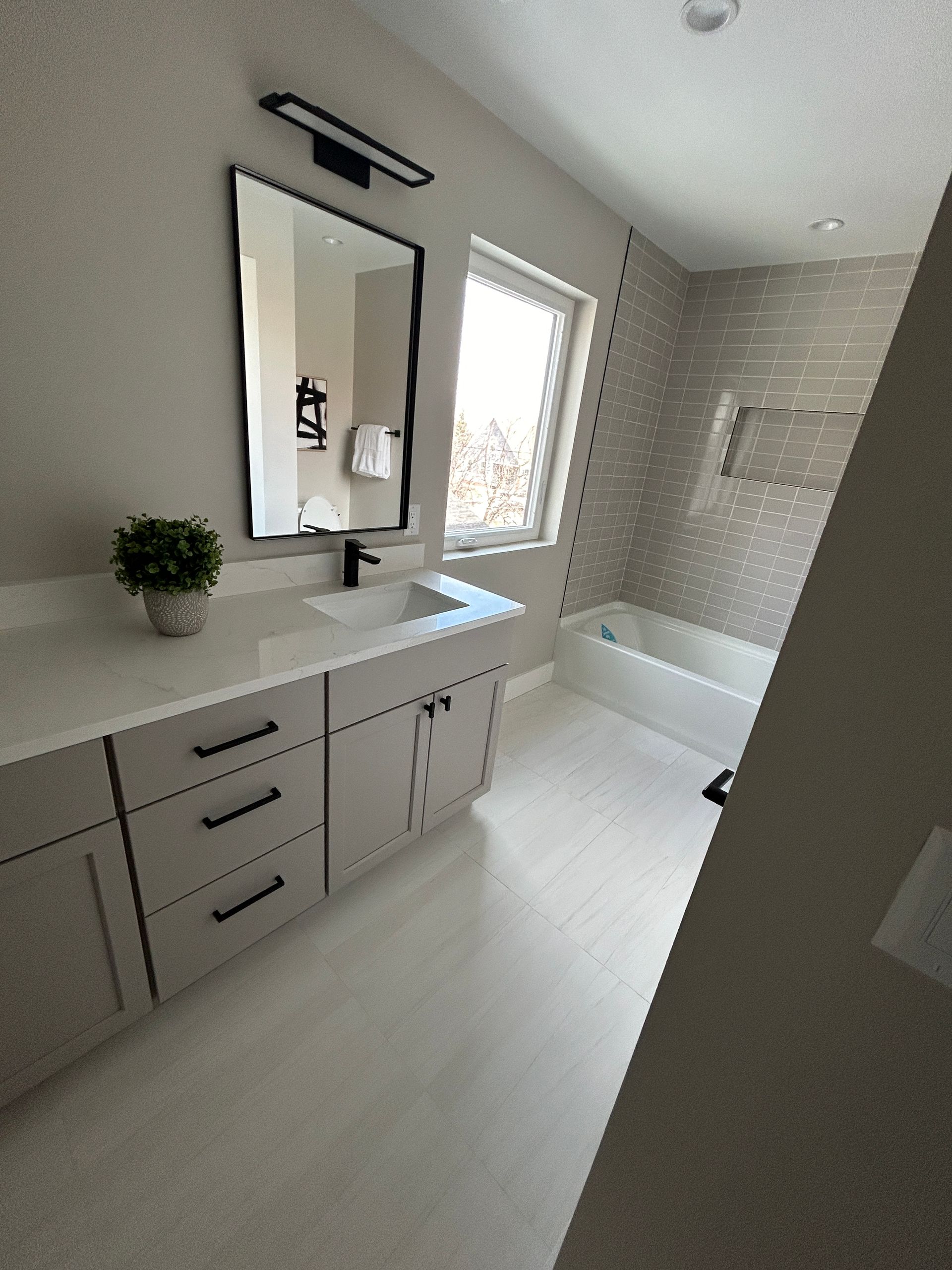 Bathroom with light gray cabinets, white countertop, large mirror, and tub.