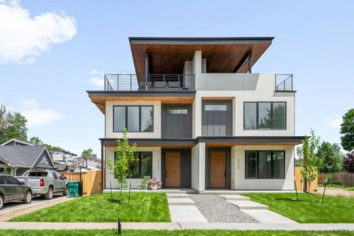 Modern two-story duplex with flat roof, balconies, and light wood accents. Green lawn and blue sky.