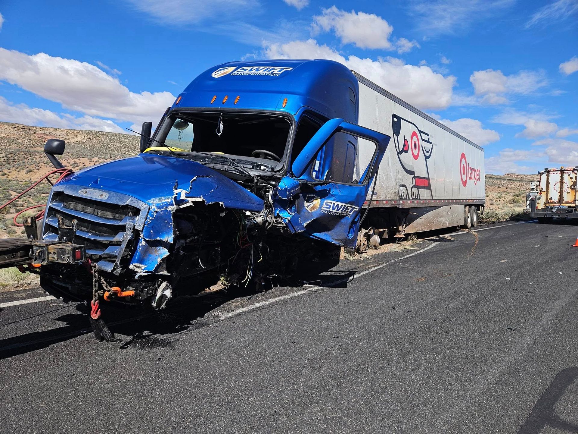 Damaged blue semi-truck on a highway, Chick-fil-A logo on trailer, front end heavily damaged.