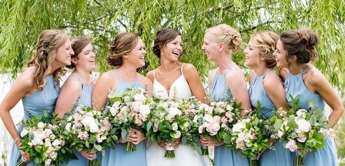 Blonde woman with updo hairstyle, wearing earrings and a white top, looking to the viewer.
