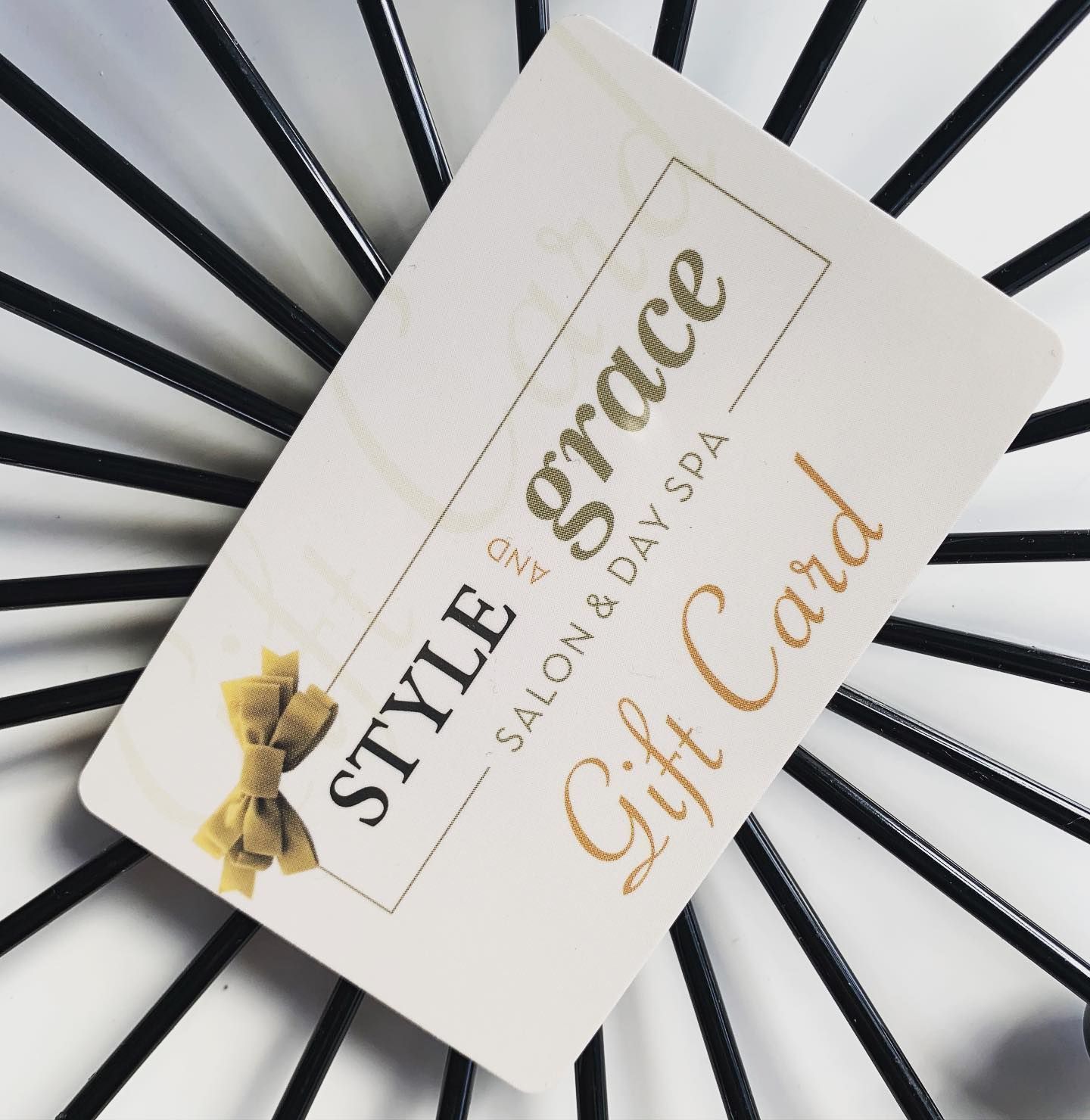 Gift card for Style & Grace Salon & Day Spa; cream card with gold text and bow on a black metal design.