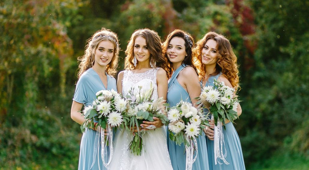 Blonde woman with updo hairstyle, wearing earrings and a white top, looking to the viewer.