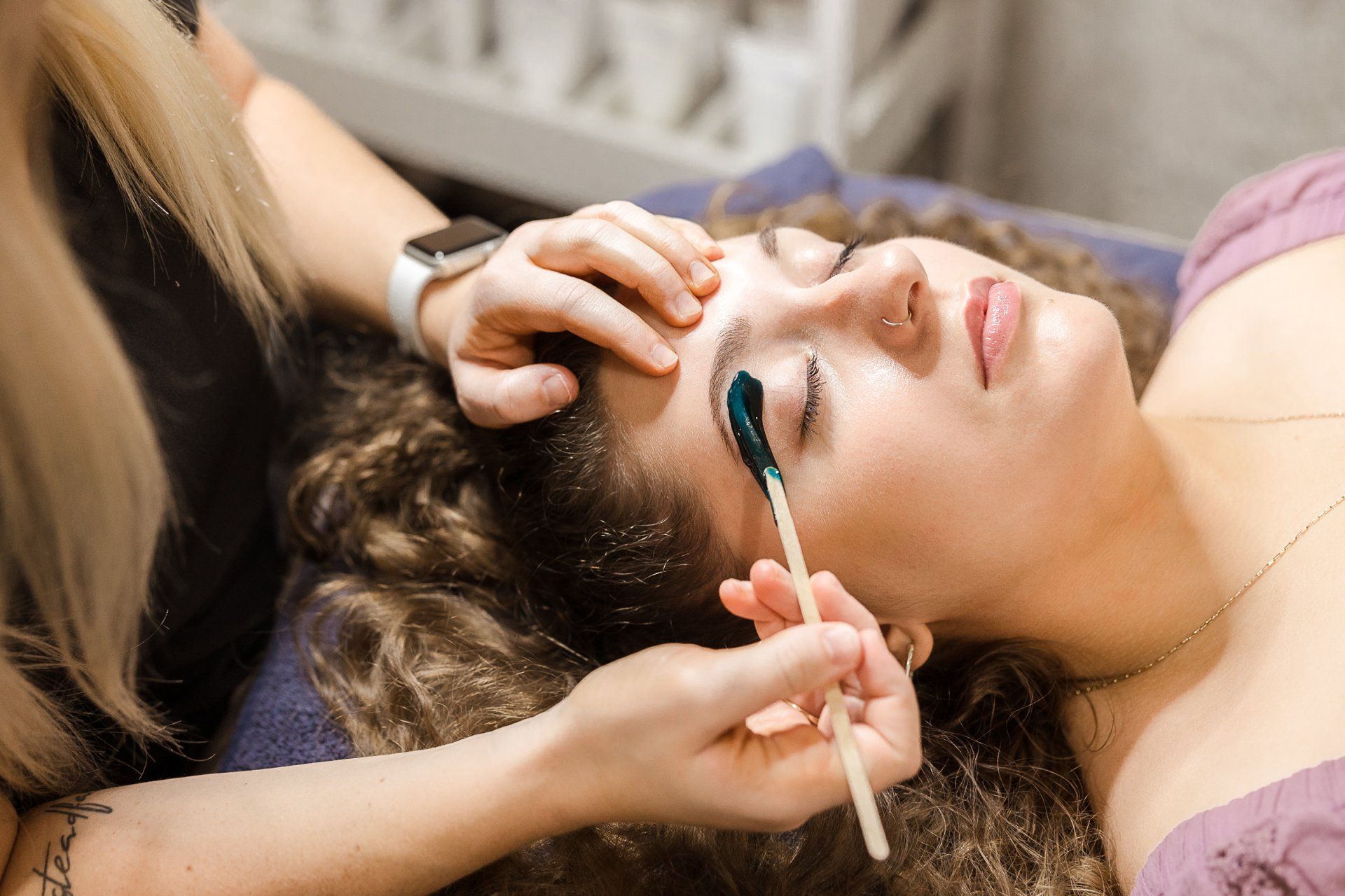 Person having eyebrow wax applied; close up. Aesthetican holding stick applying wax.