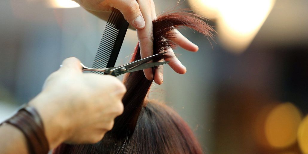 Hands cutting hair with scissors and a comb in a salon.