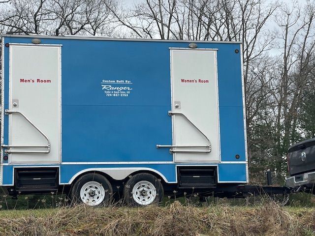 A blue and white restroom trailer is parked in a field.
