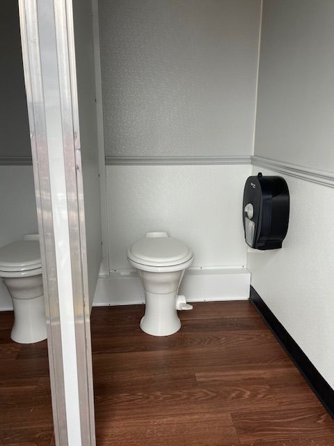 Restroom trailer with two toilets and a paper towel dispenser.