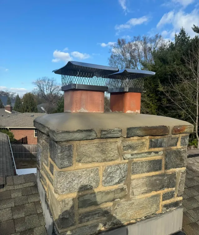 Brick chimney with two chimney pots topped with metal caps, blue sky in background.