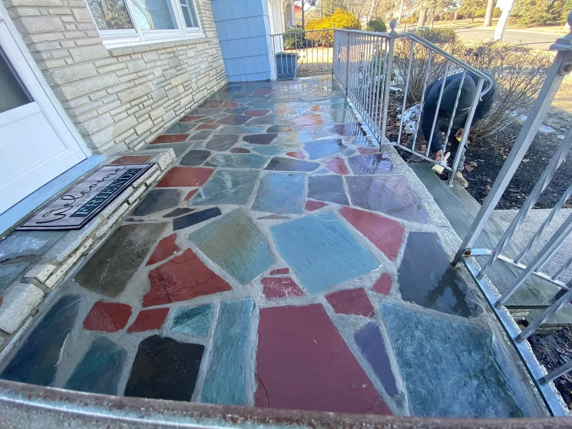 Porch with multi-colored stone tiles, metal railing, and a doormat.
