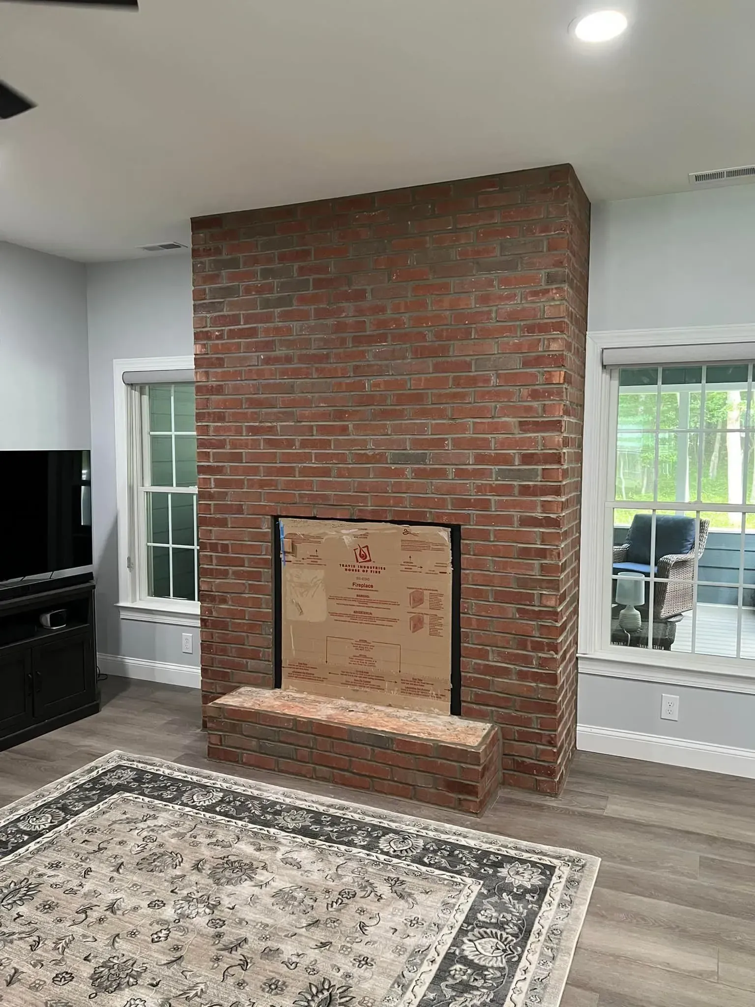 Brick fireplace in a room with windows, a rug, and entertainment center.