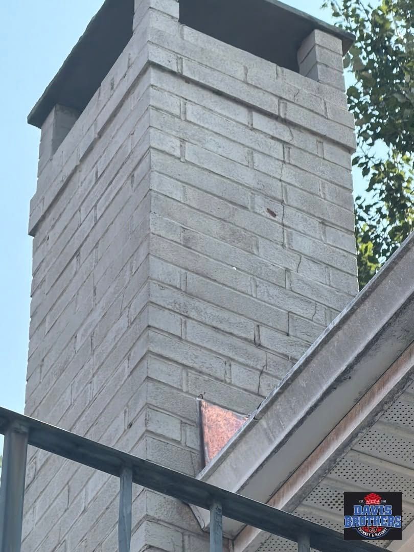 Brick chimney above a sloped roof with dark trim against the sky