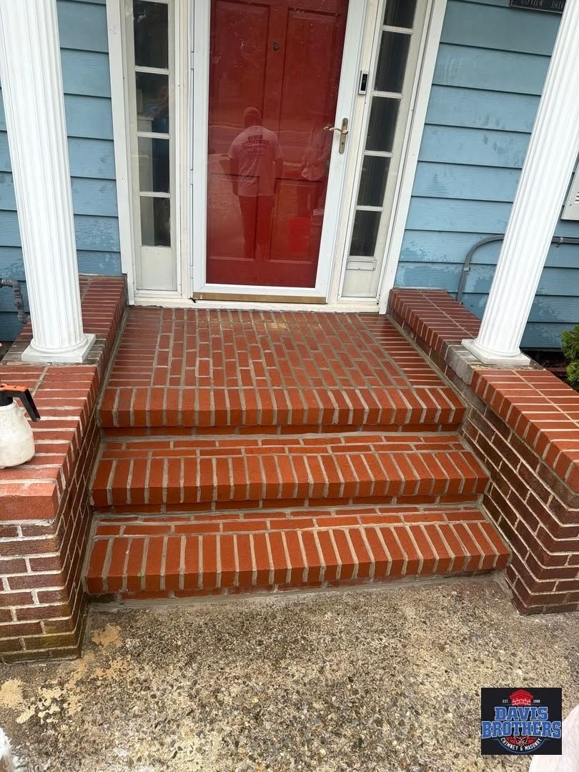 Brick front steps with a red door and white columns on a blue house porch