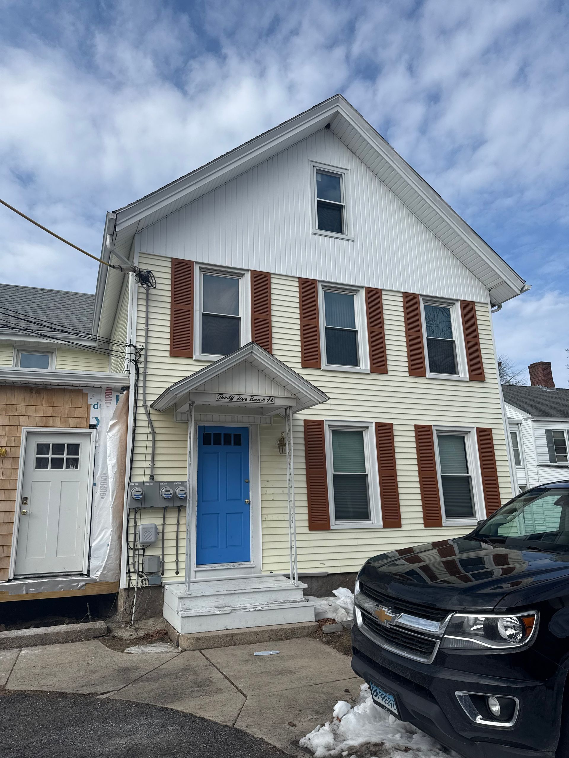 Yellow house with brown shutters, blue door, and a black SUV parked in front.