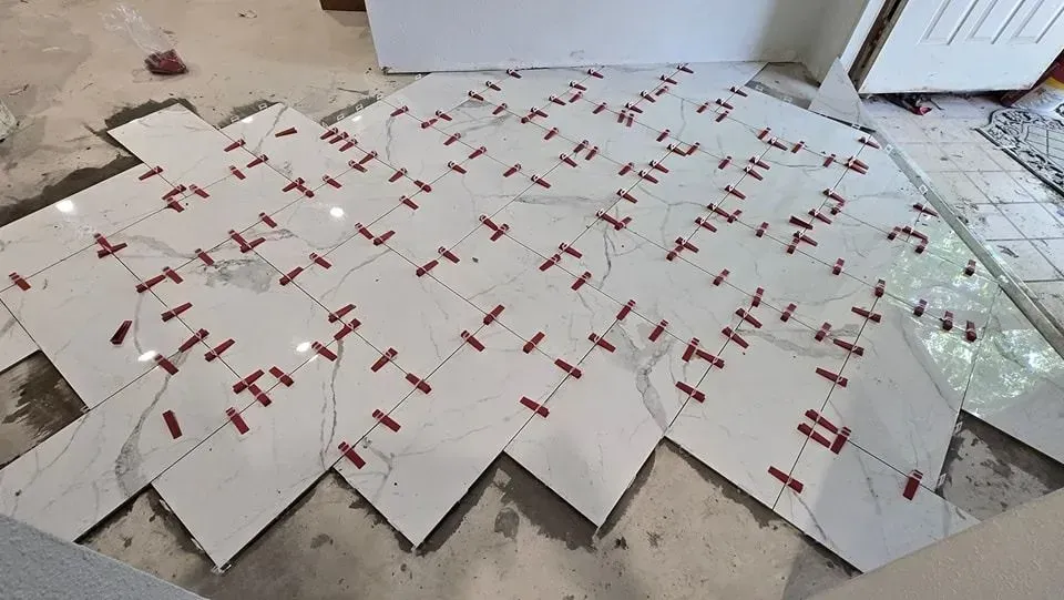 Tiles being laid in a zig-zag pattern on a concrete floor, red tile spacers in place.