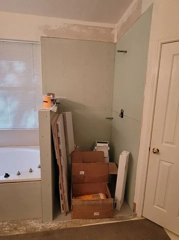 Bathroom renovation in progress; drywall and supplies next to a tub and doorway.