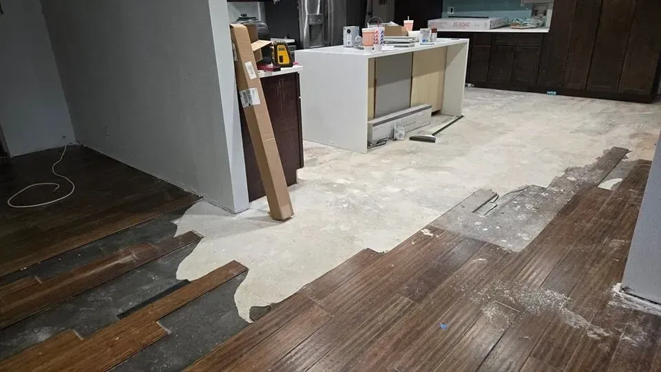 Interior with damaged wood flooring, construction materials, and a partially constructed kitchen island.