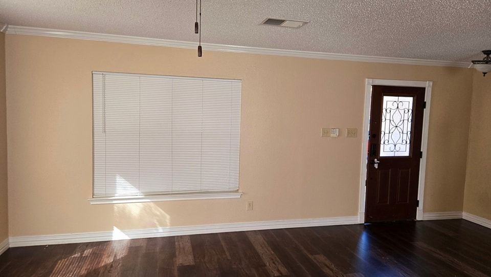 Empty room with beige walls, dark wood floor, white trim, window with closed blinds, and a dark wooden door.