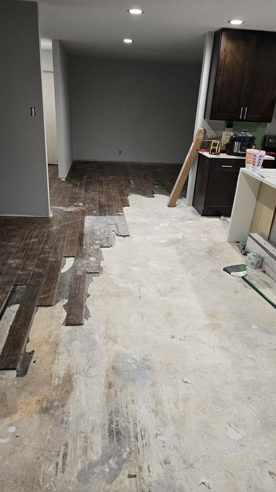 Partial floor renovation; old wood flooring being removed; grey walls; kitchen cabinets visible.