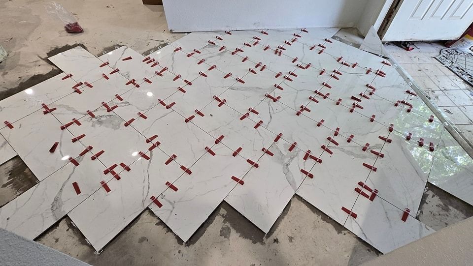 Diamond-pattern tile floor installation in progress, white tiles with red leveling clips, room interior.