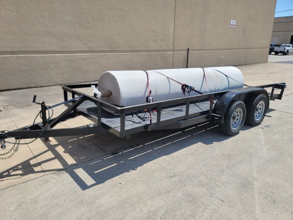 Black trailer with a large white cylindrical object secured on it, outdoors.