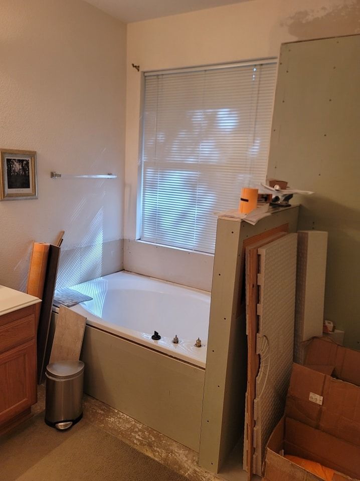 Bathroom renovation with a partially constructed tub surround. Light green drywall and construction materials nearby.