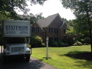 A statewide moving and storage truck is parked in front of a large brick house