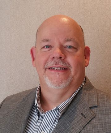 A bald man with a beard is wearing a suit and smiling.