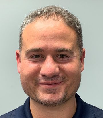 A man with a beard is smiling and wearing a blue shirt.