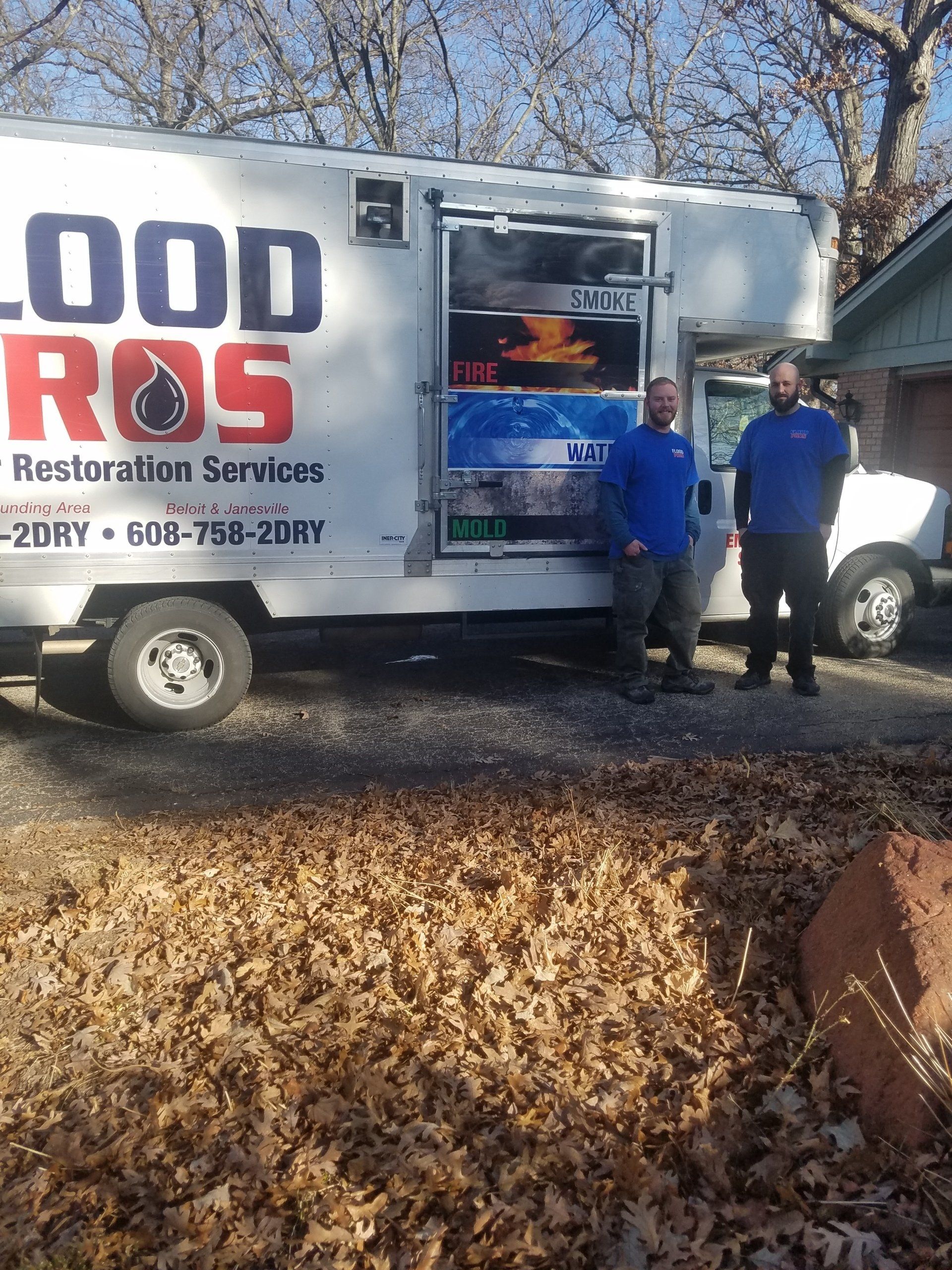 Two men stand in front of a white service truck. The truck has 