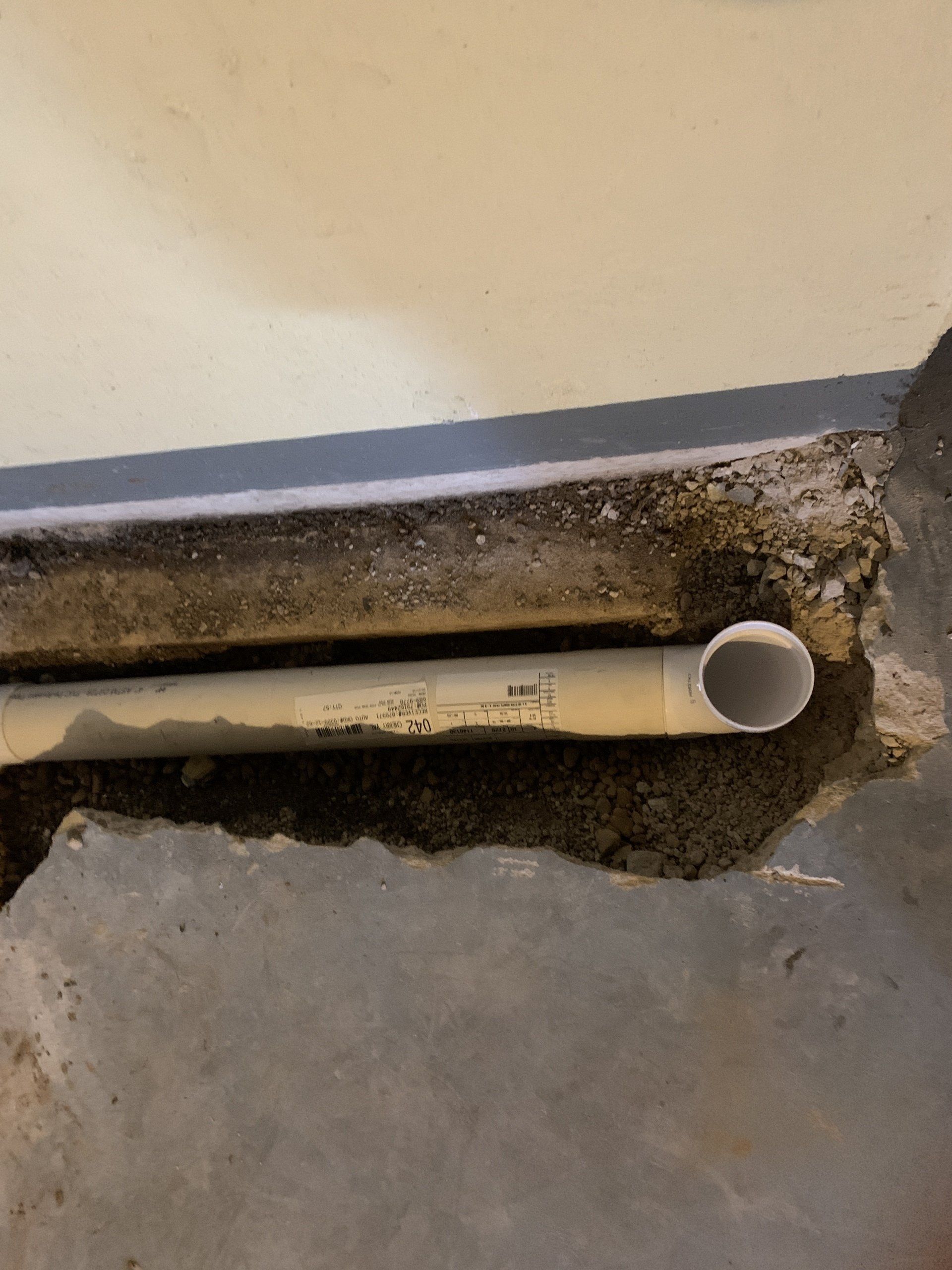 White PVC pipe exposed in concrete floor, likely for plumbing. The pipe runs along the floor near a wall.