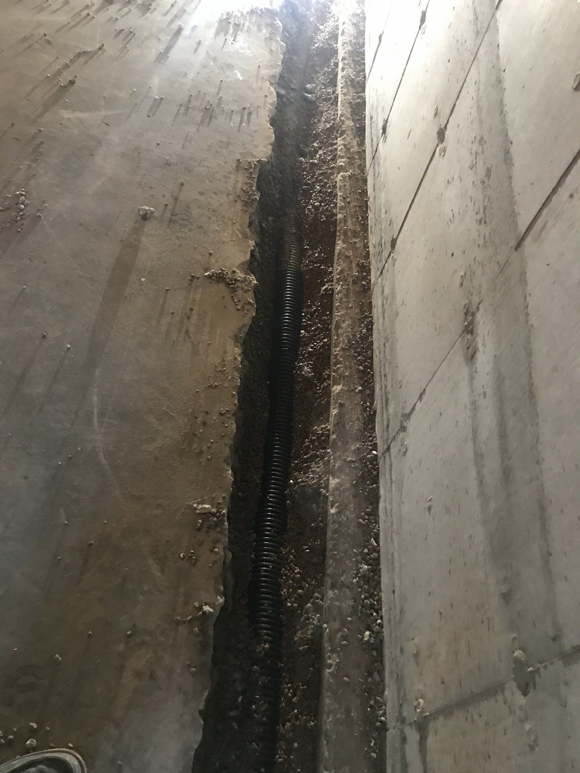 A crack between two concrete walls, with visible rebar and moisture, likely a foundation.