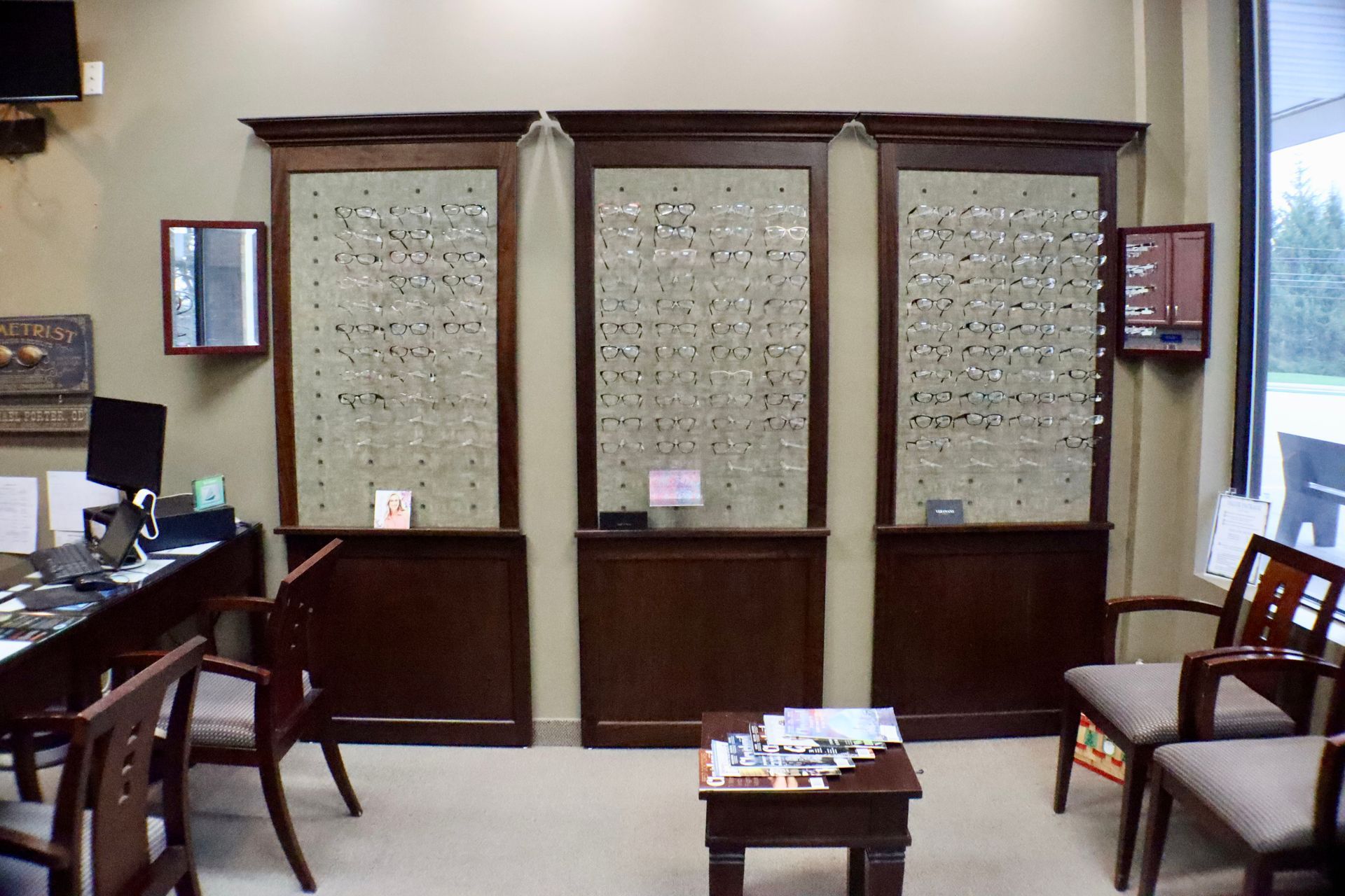 A waiting room with chairs , a table and a display of glasses.