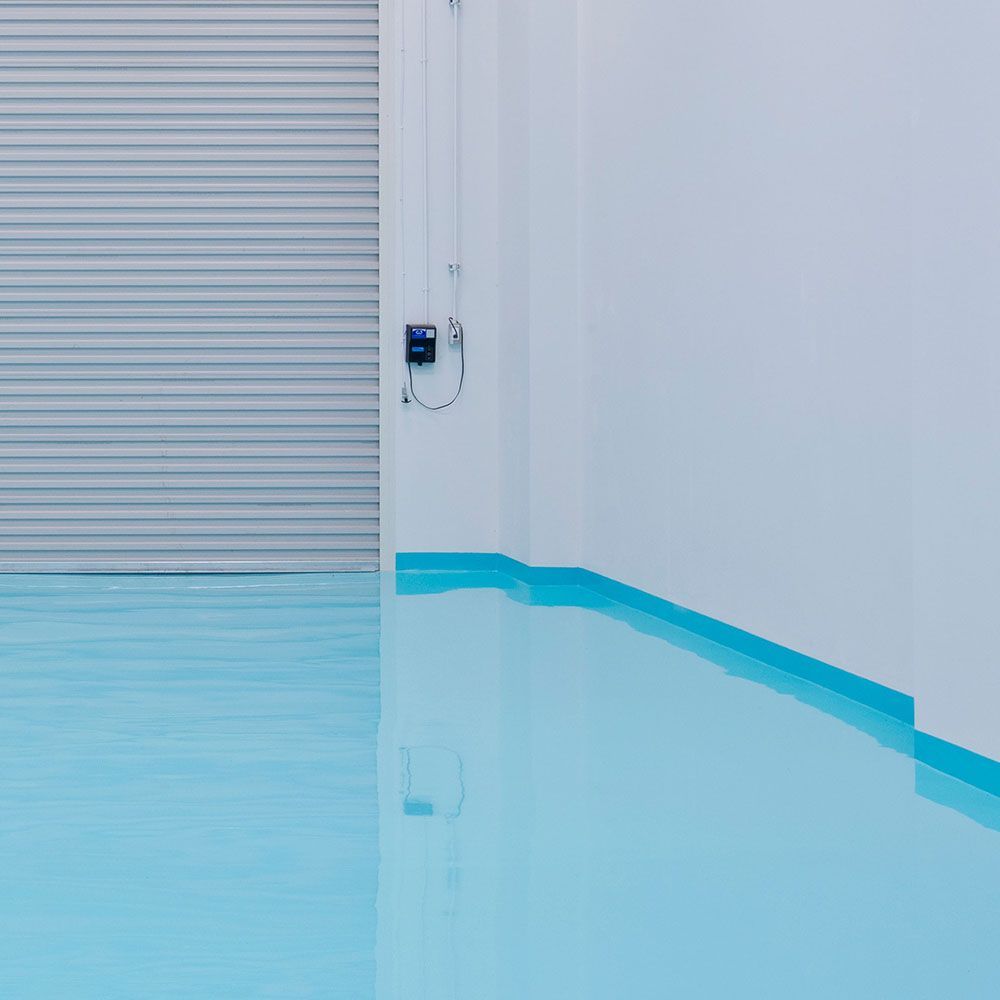 Blue epoxy floor meets a white wall with blue trim, and a gray roll-up door.