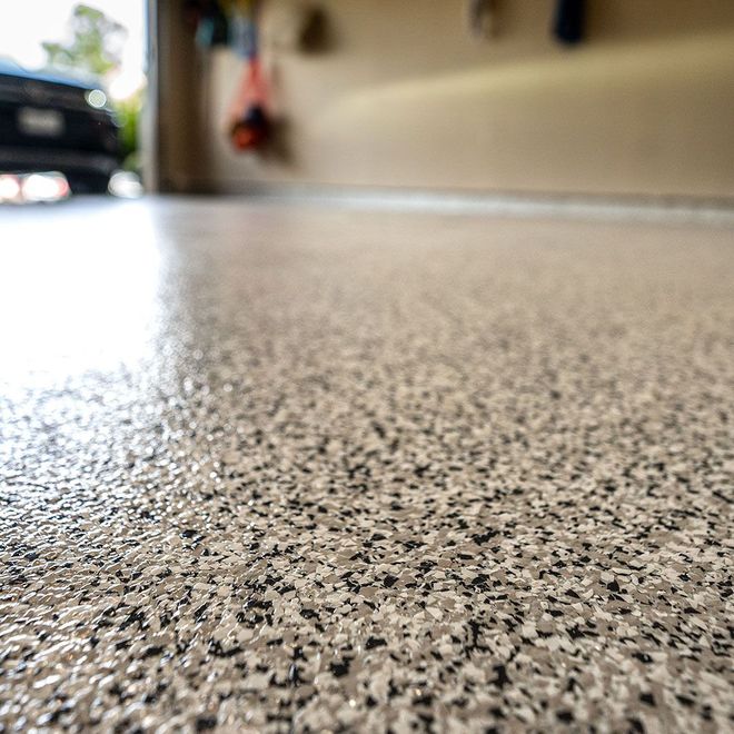 Close-up of a speckled, glossy garage floor with visible car and items hanging in the background.