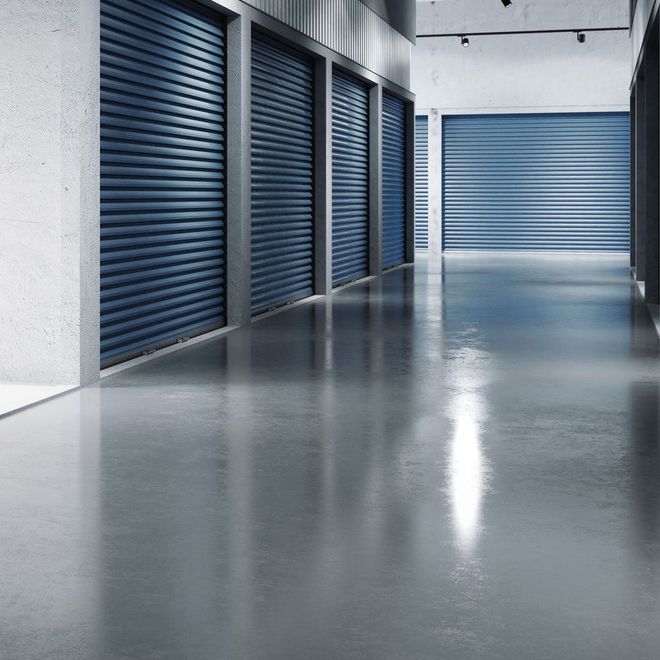A row of blue storage unit doors in a concrete hallway, reflecting light.